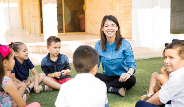 fullhd_portrait-beautiful-preschool-teacher-having-class-outdoors-with-group-students-smiling